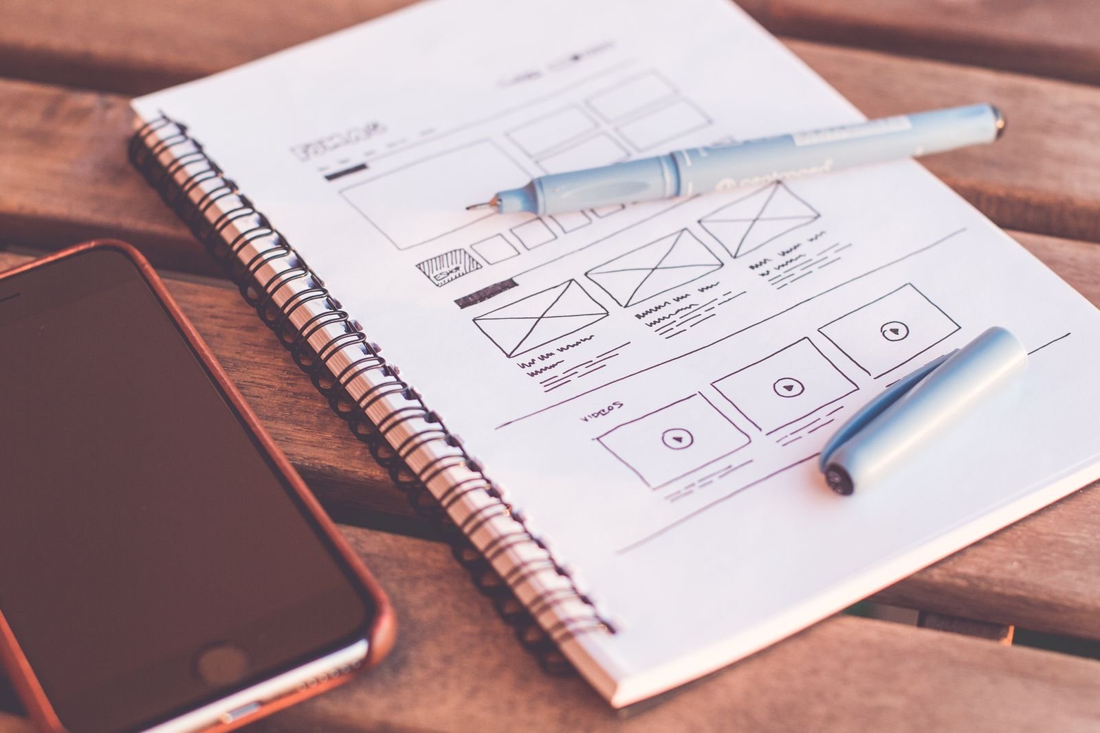 Website wireframes sketched in a notebook beside a phone