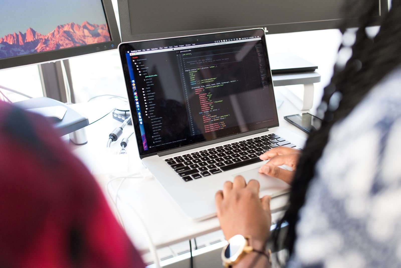 Two people writing code at a bright desk